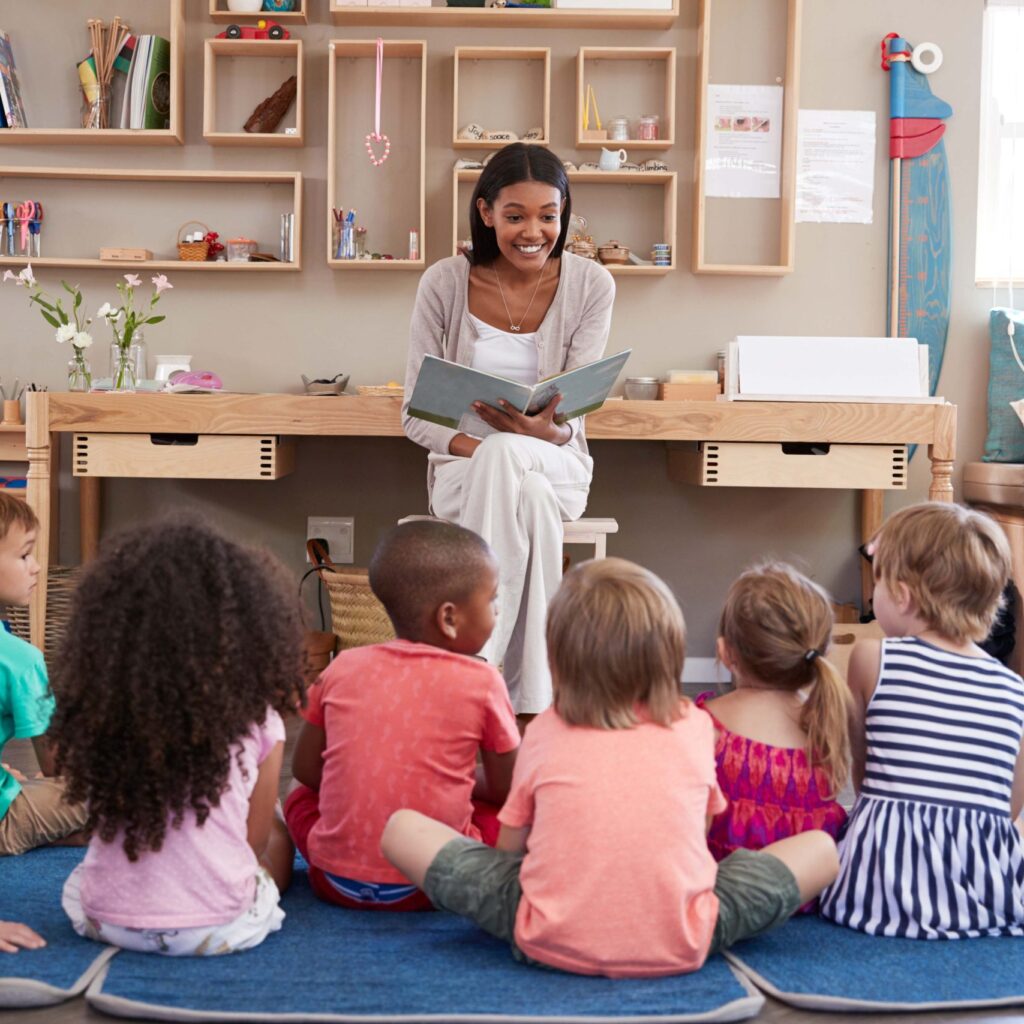 Teacher At Montessori School Reading To Children At Story Time