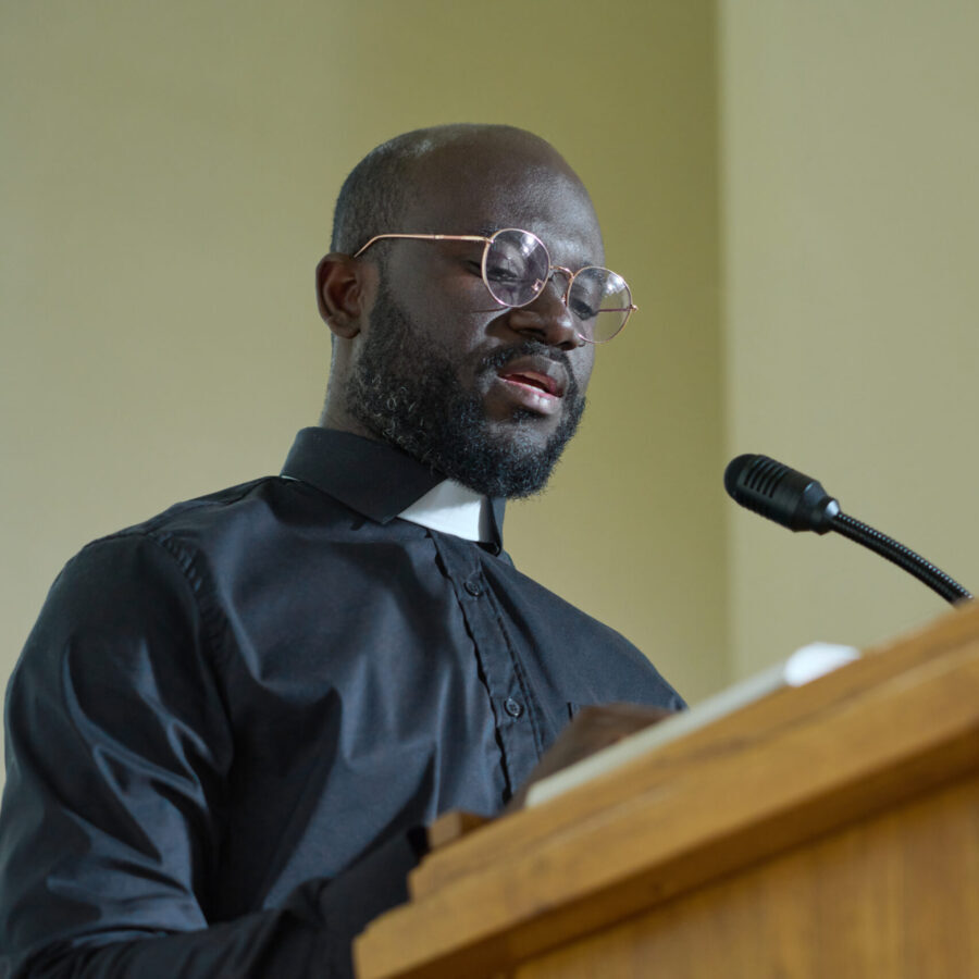 Young priest in black shirt with clerical collar pronouncing speech by pulpit