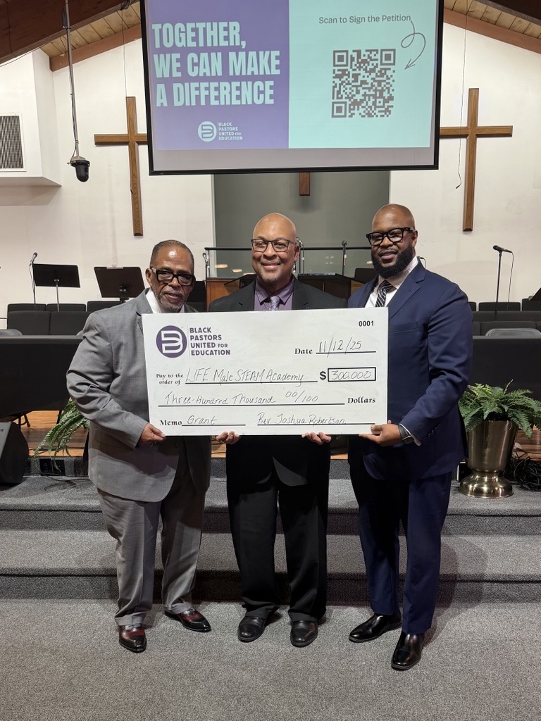 three men stand at the front of a church holding oversized ceremonial check from Black Pastors United for Education, with a screen behind them reading "Together we can make a difference" and displaying a QR code.